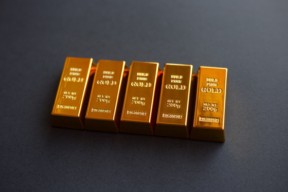 Fünf glänzende Goldbarren nebeneinander auf dunklem Untergrund, Nahaufnahme.