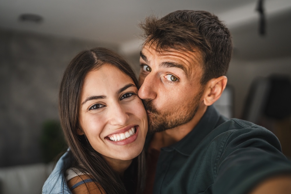 Nahaufnahme eines jungen Paares, das sich umarmt; der Mann küsst die Frau auf die Wange.
