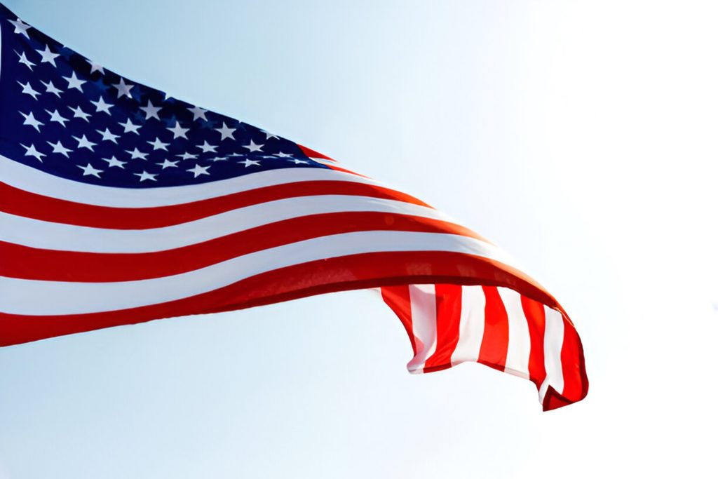 Im Wind wehende US-Flagge vor hellem Himmel, Nahaufnahme der Sterne und Streifen.