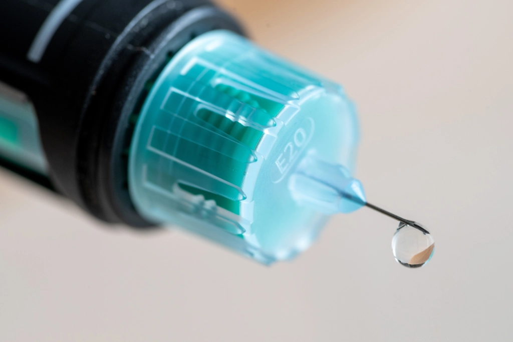 Nahaufnahme einer medizinischen Spritze mit transparenter Flüssigkeit an der Kanülenspitze.