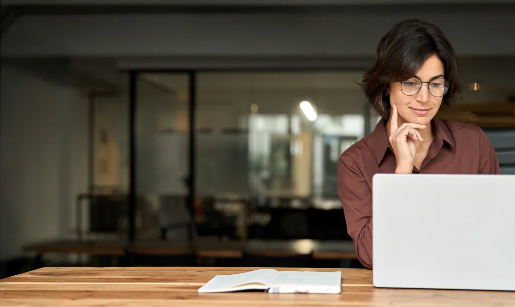 Selbstbewusste Geschäftsfrau arbeitet mit Laptop und Notizbuch in einem modernen Büro – Konzept für Finanzplanung und strategisches Money Management im Financipation Club