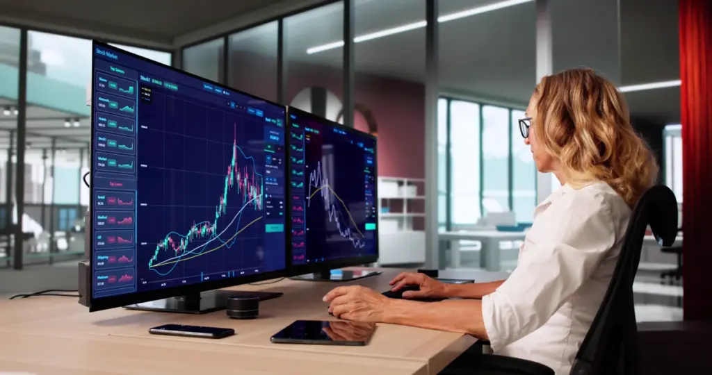 Person analysiert Börsendaten auf mehreren Bildschirmen in einem modernen Trading-Setup – Financipation Club